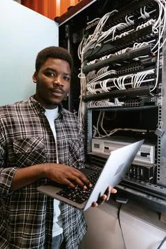 Man working on a laptop in a server room during daylight hours, managing Stock Photos