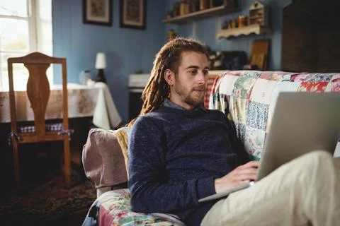Man working on laptop sitting on patchwork sofa in cozy home with decorative Fotos de archivo