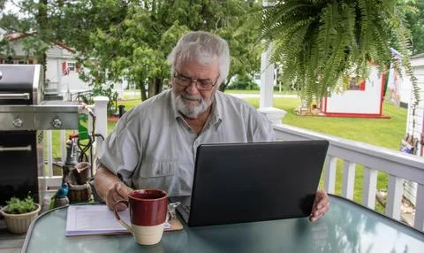 Man Working on Laptop While Drinking Coffee on Porch During Sunny Day Stock Photos