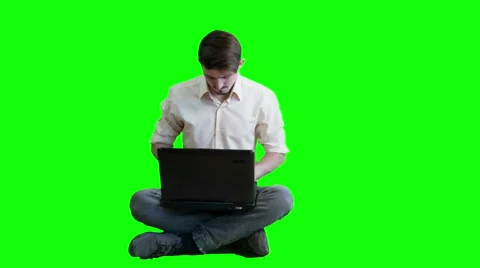 A man  working on a laptop while sitting on a background of a green scre Stock Footage 47260531
