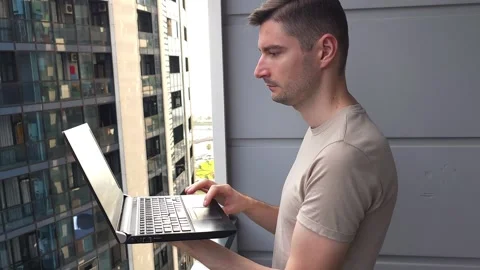 Man working on a laptop while standing on a balcony. Success and business Stock Footage 284042514