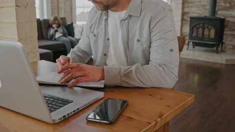 Man working at the laptop, writing notes at home because of covid restrictions Видео 165413720