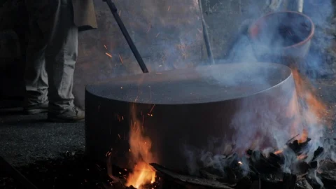 Man working with a large copper pot over an open flame in slow motion Video stock 98843676