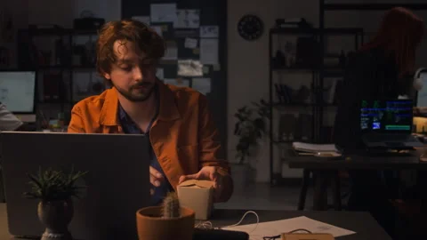 Man Working Late on Laptop in Office Opening Takeout Food Box Stock Footage 338417836