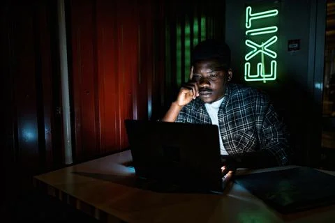 Man working late at night in a dimly lit room with an exit sign nearby Stock Photos