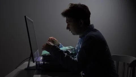 Man working late at night, illuminated by a computer screen, handling documents Vidéo 342671582