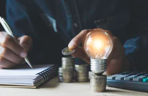 Man working with a light bulb on stack of coins for business and accounting c Stock Photos