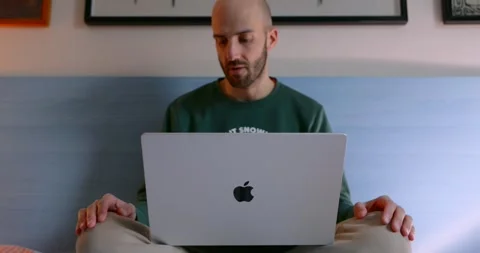 Man working on MacBook laptop while sitting on bed Stock Footage 335967226