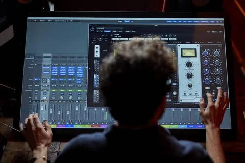 Man working in music studio using large computer screen shot from behind Foto stock
