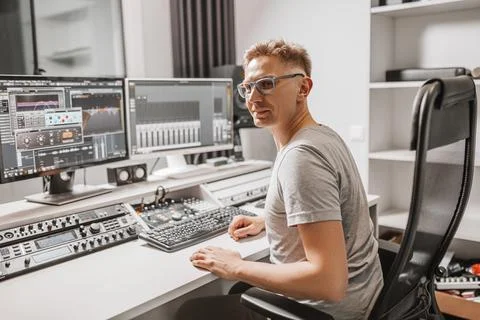 Man working in music studio using computer wearing glasses. Sound engineer wo Stock Photos