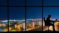 The man working near a panoramic window on a night city background. time lapse 4k or 4k+ Resolution