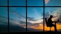The man working near a panoramic window on a mountain sunset background 4k or 4k+ Resolution