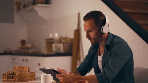 Man working at night on his kitchen using tablet and listen to music with Stock Footage 168626564