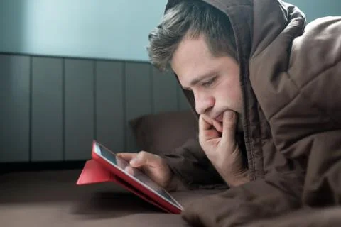 Man is working at night, lying on the sofa in the living room with tablet Stock Photos