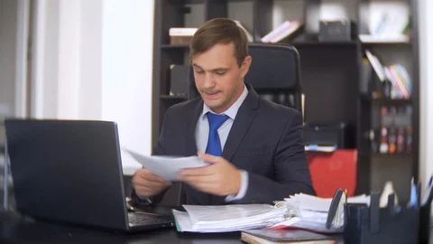 Man working in office with documents. he looks at the camera and smiles Stock Footage 88100072