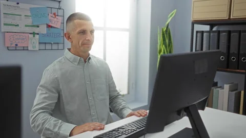 Man working in office, using computer, dressed in light shirt, surrounded b.. Stock Footage 285093176