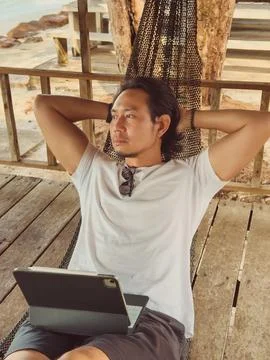 Man working online with computer on the hammock by the beach. Stock Photos