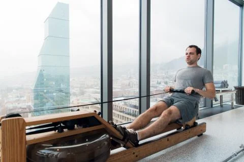 Man working out on row machine in fitness studio at scyscraper luxury hotel gym Stock Photos
