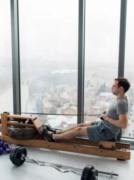Man working out on row machine in fitness studio at scyscraper luxury hotel gym Stock Photos