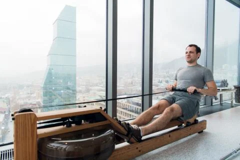 Man working out on row machine in fitness studio at scyscraper luxury hotel gym Stock Photos