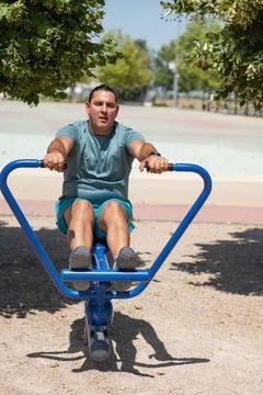 Man working out on a rowing machine in a park Stock Photos