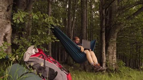Man working outdoors with laptop in hammock Stock Footage 133328873
