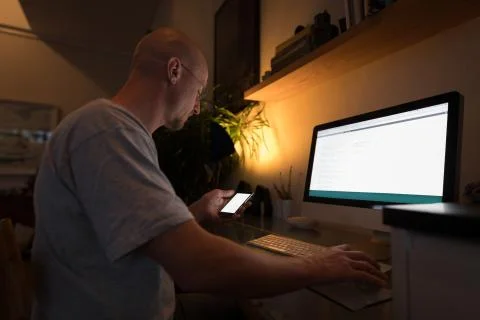 Man working on personal computer while using mobile phone Foto stock