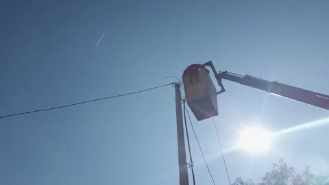 A man is working on a power line with a bucket truck. The sky is clear and br Stock Footage 344916036