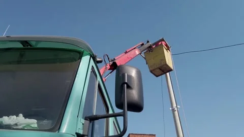A man is working on a power line with a bucket truck. The sky is clear and br Stock Footage 344916039