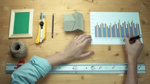 Man working with printed graphs making notes with marker at wooden desk. Video stock 82901937