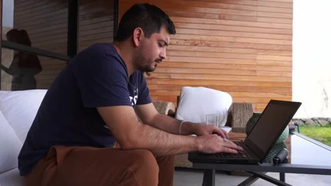 A man working remotely with his laptop on the terrace and his brother coming to Stock Footage 199490466