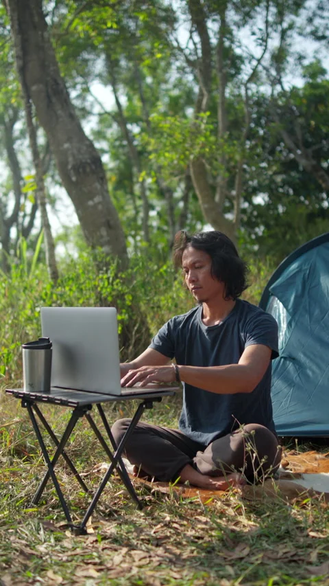 Man working remotely on a laptop beside a tent Stock Footage 341770865
