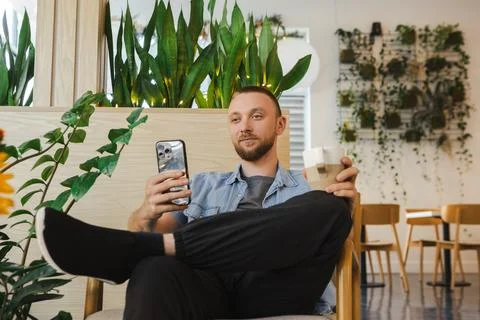 Man working remotely in a modern cafe while using a smartphone and enjoying.. Foto stock
