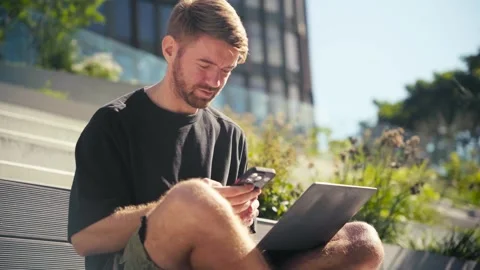 Man working remotely, sitting on sunlit public stairs with laptop on his knees. Stock Footage 316254113