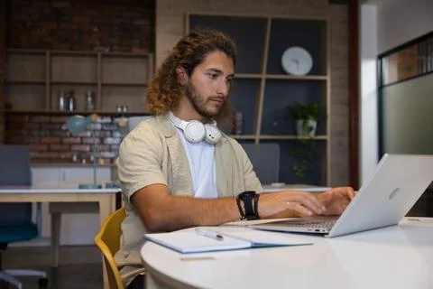 Man working on silver laptop at modern co-working table with notebook, pen and Photos
