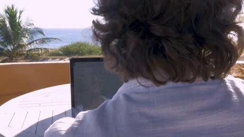Man working on spreadsheet on computer at home with ocean view dolly shot Stock Footage 80136732