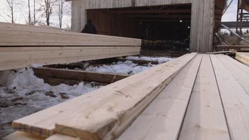 Man working at stacks of packed lumber stored in yard of sawmill Stockbeeldmateriaal 86012126