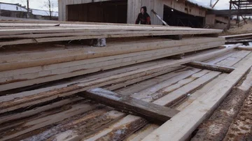 Man working at stacks of packed lumber planks stored in yard of sawmill Stockbeeldmateriaal 86012370