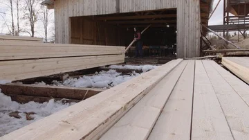 Man working at stacks of packed wooden boards stored in yard of sawmill Stockbeeldmateriaal 86011914