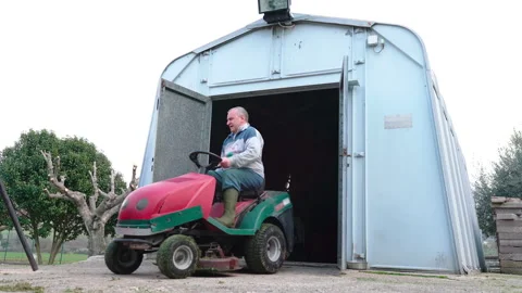 Man in working suit driving out from private garage on lawn tractor Stock Footage 208024782
