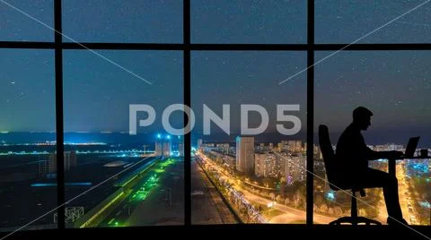 The man working at the table near a panoramic window with a night city view Stock Photos
