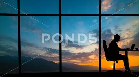 The man working at the table near a window on a mountain sunset background Stock Photos