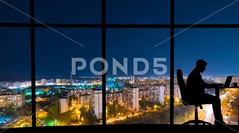 The man working at the table near a window with a night city view Stock Photos