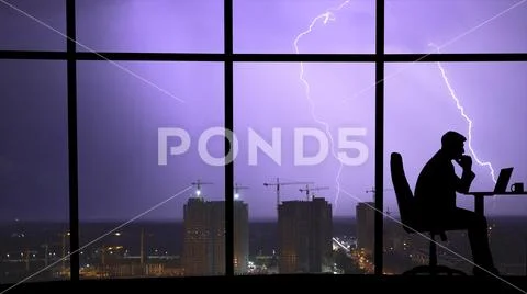 The man working at the table near a window on a city lightning background Stock Photos