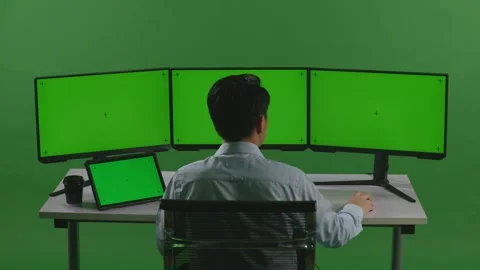 Man Working With Tablet And Multiple Computer Monitor With Mock Up Green Screen Stock Footage 249625054