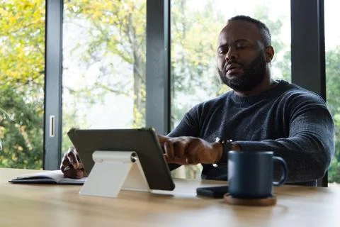 Man working on tablet on white stand at wooden table with notebook and Stock Photos