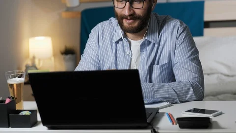Man working talking on video connection and drinks beer. Bearded guy sits at Stock Footage 129382954