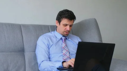 Man working typing on laptop at home sitting on couch, freelance distant work. Stock Footage 128965574
