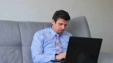 Man is working typing on laptop at home sitting on couch and falling asleep. Stock Footage 128965808