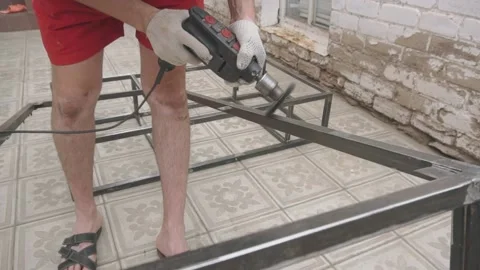 A man in working uniform holds a drill in his hands, which are wearing gloves Vidéo 145182219